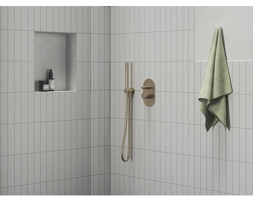Moderní sprcha s úzkými obklady, podomítkovou baterií, tyčovou ruční sprchou a nikou v minimalistické koupelně.