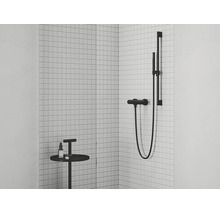 Moderní sprchová baterie se sprchovou tyčí a ruční sprchou v minimalistickém designu před stěnou z bílých mozaikových dlaždic v koupelně.