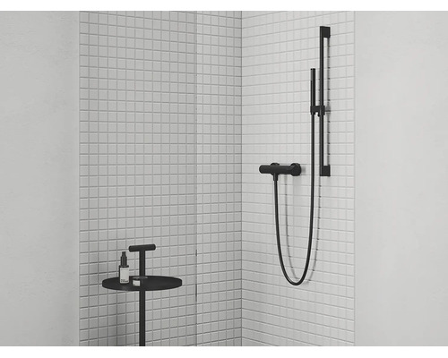 Moderní sprchová baterie se sprchovou tyčí a ruční sprchou v minimalistickém designu před stěnou z bílých mozaikových dlaždic v koupelně.