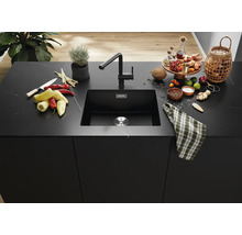 Moderní černý kuchyňský dřez s odpovídající baterií na elegantním kamenném kuchyňském ostrůvku s ingrediencemi na vaření a dekoracemi.