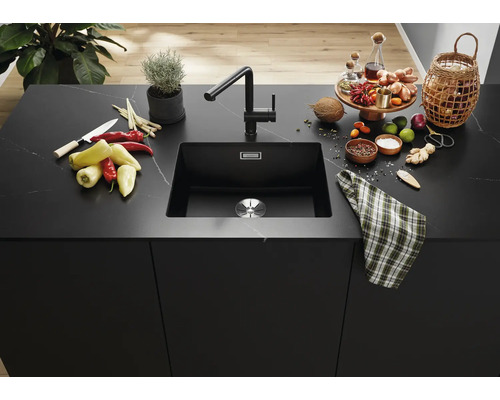 Moderní černý kuchyňský dřez s odpovídající baterií na elegantním kamenném kuchyňském ostrůvku s ingrediencemi na vaření a dekoracemi.