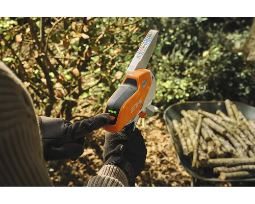 Osoba používá akumulátorovou pilu na větve Stihl s LED indikátorem nabití v zahradním prostředí