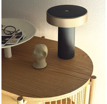 Moderní dobíjecí lampa na kulatém dřevěném odkládacím stolku s dekorativními předměty.
