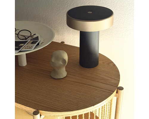 Moderní dobíjecí lampa na kulatém dřevěném odkládacím stolku s dekorativními předměty.