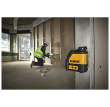 Křížový laser DeWalt promítá zelenou laserovou linku na staveništi, kde pracuje řemeslník.