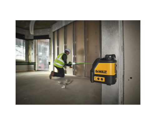 Křížový laser DeWalt promítá zelenou laserovou linku na staveništi, kde pracuje řemeslník.