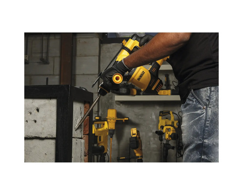 Osoba používá vrtací kladivo DeWalt k opracování betonu, přičemž v dílně jsou vidět další elektrické nástroje.