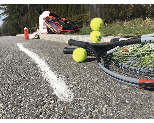 Tenisové rakety, tenisové míčky, tenisová taška a láhev na pití na asfaltu