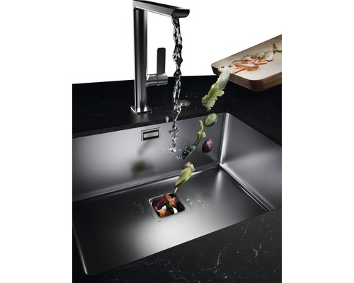 Kuchyňský dřez s drtičem odpadu, vodovodní baterií a padajícími zbytky zeleniny