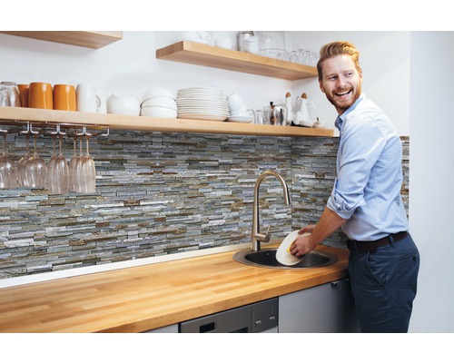 Stěnový obklad PVC Ceramics StoneWall bl-gr. KR 67,5x400 cm Kuchyňská scéna s kamennými obkladovými panely, dřezem a mužem myjícím nádobí
