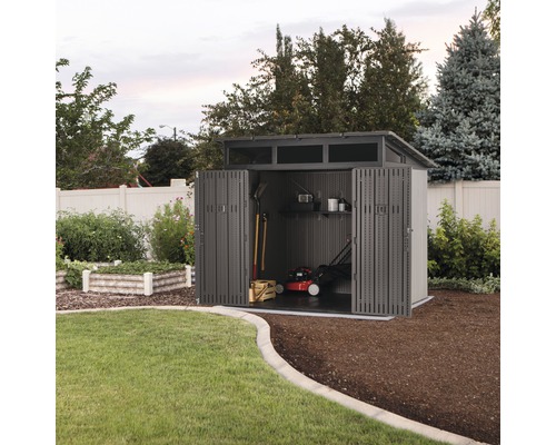 Zahradní kůlna s otevřenými dveřmi, uvnitř sekačka na trávu a zahradní nářadí.