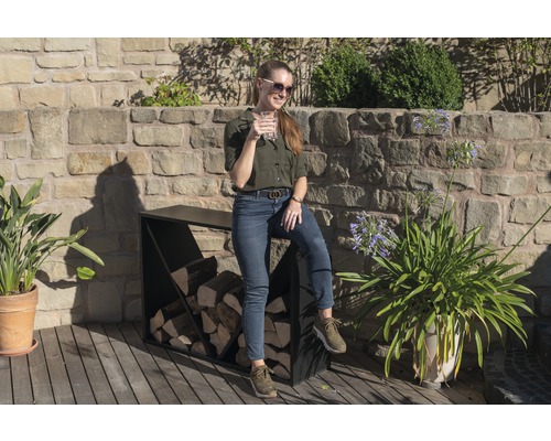 Žena sedí na venkovním stojanu na palivové dřevo s kamennou zdí v pozadí.