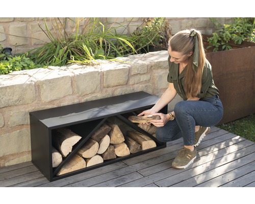 Žena vkládá dřevo do černé police na dřevo v zahradě