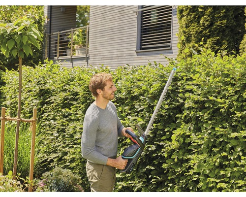 Muž stříhá živý plot nůžkami na živý plot na zahradě.