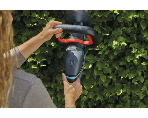 Osoba používá akumulátorové nůžky na živý plot Gardena před živým plotem.