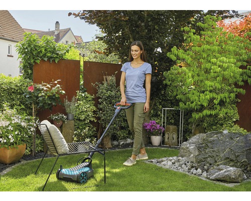 Žena seče trávník sekačkou na trávu na zahradě.