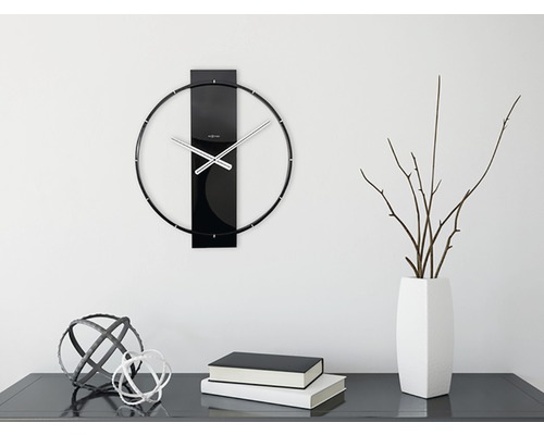 Nástěnné hodiny s kovovými ručičkami a dekorací na komodě