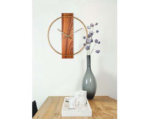 Nástěnné hodiny s dřevěnými detaily a zlatými akcenty nad dřevěným stolem s dekoracemi.