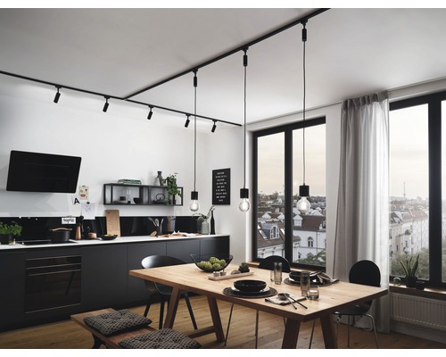 Světlá kuchyně s jídelním stolem, židlemi a černým kuchyňským koutem pod kolejnicovým osvětlením