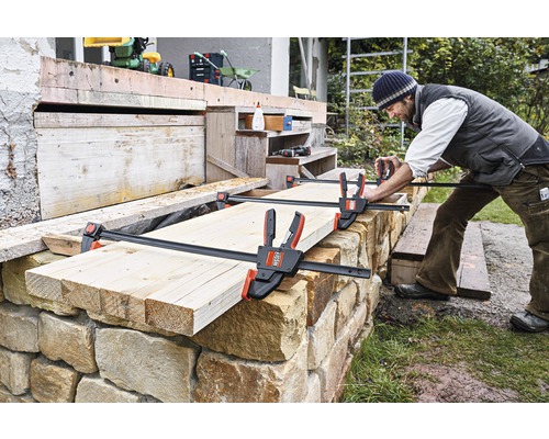 Řemeslník upevňuje dřevo k zděné zdi pomocí horizontální jednoruční svěrky.