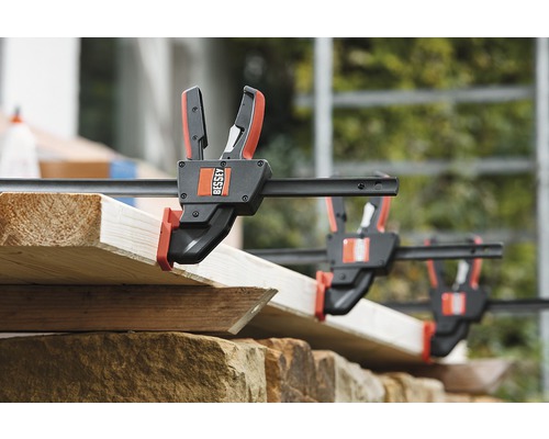 Několik šroubových svěrek upevňuje dřevěné desky. Logo Bessey.