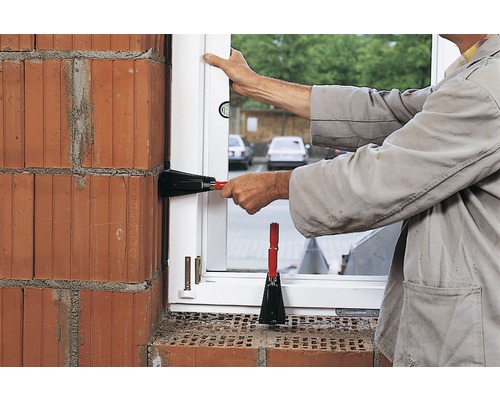 Řemeslník montuje okno s okenními zvedáky do cihlové zdi.