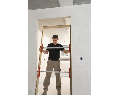 Muž montuje zárubeň dveří pomocí rozpěrky dveří v hrubé stavbě.