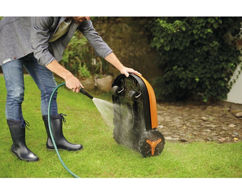 Muž čistí robotickou sekačku hadicí na trávníku.