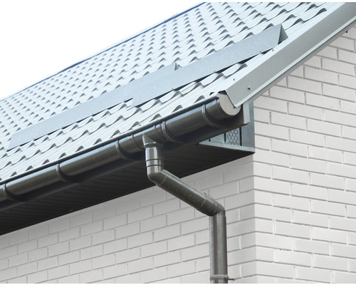 Střešní okap a svod u domu s taškovou střechou a bílou cihlovou fasádou.