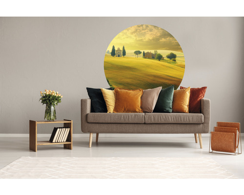 Obývací pokoj s šedou pohovkou, polštáře v různých barvách, nástěnná samolepka s motivem krajiny, dřevěný stůl s vázou a stojan na časopisy