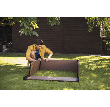 Muž sestavuje vyvýšený záhon na zahradě.