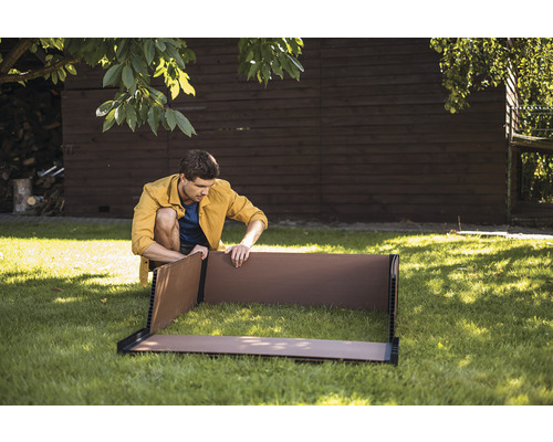 Muž sestavuje vyvýšený záhon na zahradě.