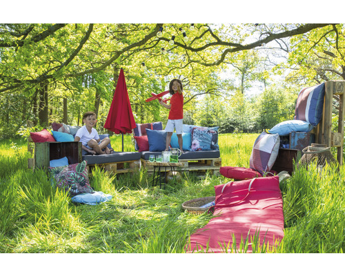 Na zahradě je posezení z palet s polštáři, slunečník a dvě děti.