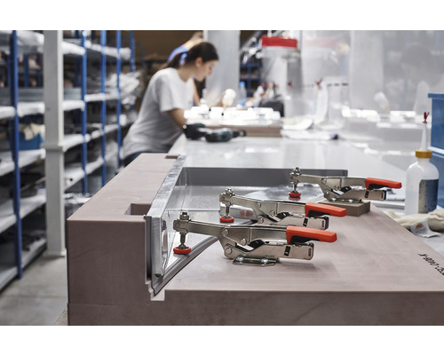 Dílenské prostředí s pracovním stolem, svorkami a osobou v pozadí