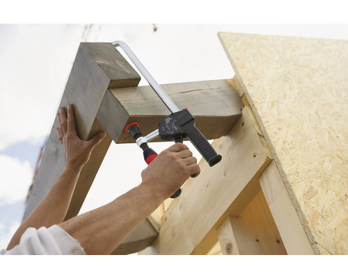 Muž upevňuje dřevěnou konstrukci šroubovou svorkou