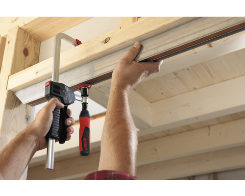 Muž připevňuje kovový profil ke dřevěné konstrukci pomocí šroubové svorky