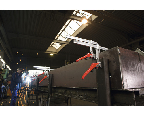 Svářeč pracuje na kusu kovu, který je upevněn pomocí rychloupínacích svorek.