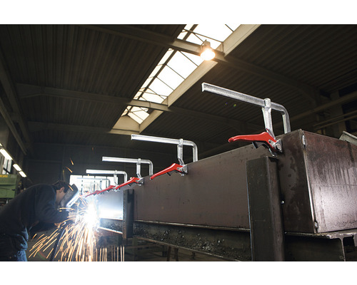 Svářeč pracuje na kusu kovu, který je upevněn rychloupínacími svorkami.