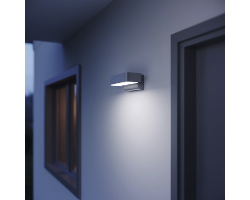 Moderní venkovní nástěnné svítidlo osvětluje stěnu domu vedle okna a dveří.