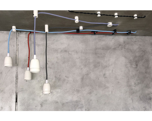 Dekorativní závěsná svítidla s textilními kabely a stropními úchyty na betonovém stropě.