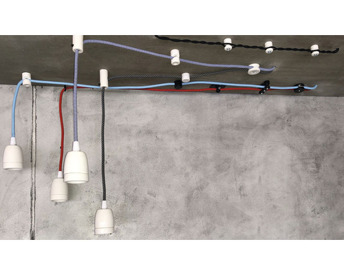 Několik závěsných svítidel s barevnými textilními kabely a bílými objímkami na betonovém stropě