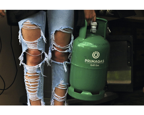 Žena v roztrhaných džínách drží zelenou plynovou láhev na grilování značky Primagas