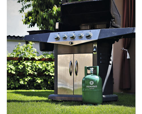 Plynový gril s ocelovým pouzdrem a zelenou plynovou lahví na trávníku