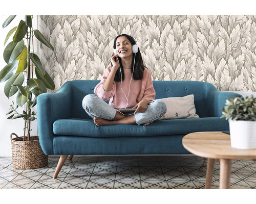 Žena se sluchátky sedí na pohovce před tapetou se vzorem listů