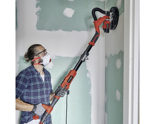 Muž brousí stěnu pomocí brusky na sádrokarton