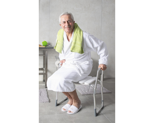 Muž sedí na sprchové stoličce s područkami v koupelně.