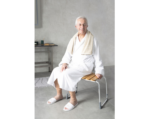 Muž sedí v koupelně na sprchové lavici s dřevěnými lamelami a hliníkovým rámem