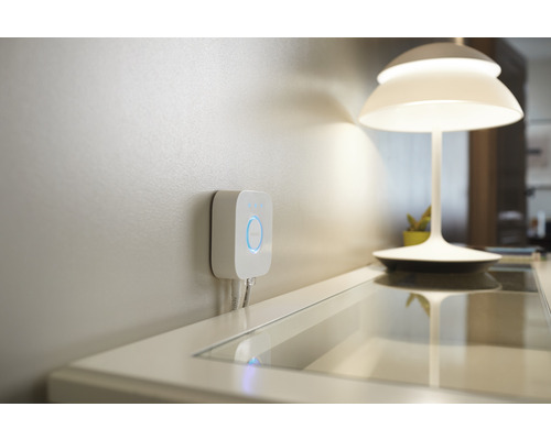 Philips Hue Bridge pro ovládání chytrého domácího osvětlení namontovaná na zdi, vedle stolní lampy.