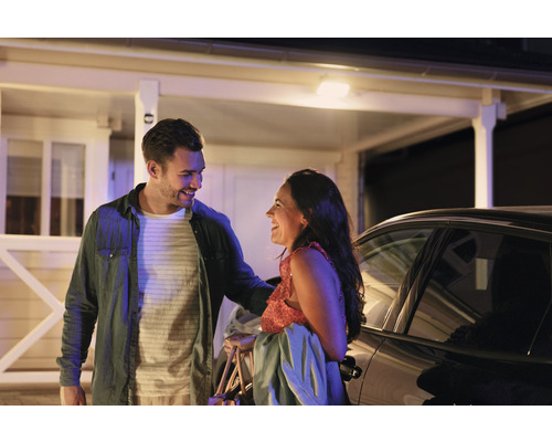 Pár se směje před domem a autem.