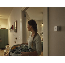 Žena nese koš na prádlo chodbou, na stěně je namontován chytrý detektor pohybu.